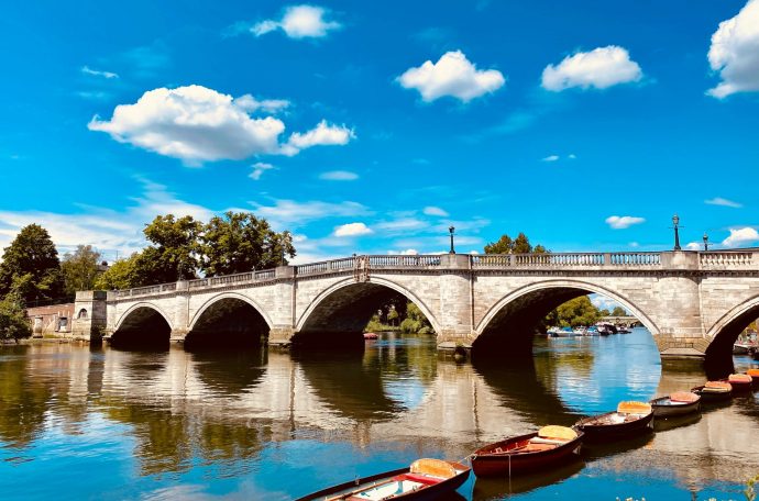 A photo of Richmond Bridge with small boats in front, and a blue sky with clouds