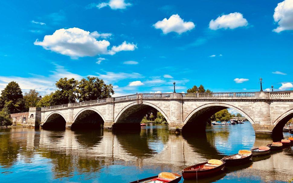 A photo of Richmond Bridge with small boats in front, and a blue sky with clouds