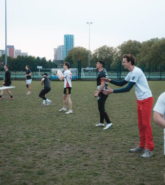 A line of frisbee players throwing frisbees on a grass pitch.