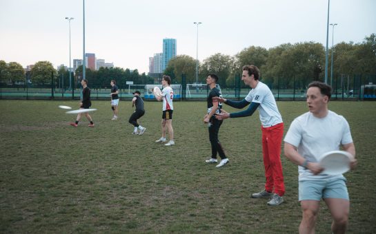 A line of frisbee players throwing frisbees on a grass pitch.