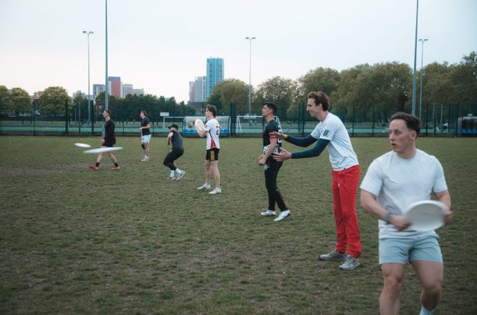 A line of frisbee players throwing frisbees on a grass pitch.