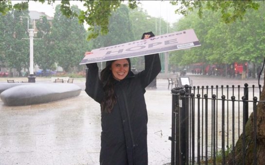 A Refuge campaigner shields herself from the torrential rain with her large 'Hope' sign.