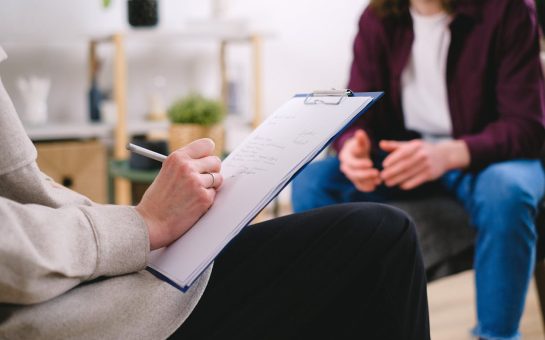 Writing notes on a clipboard while conversing with a patient.