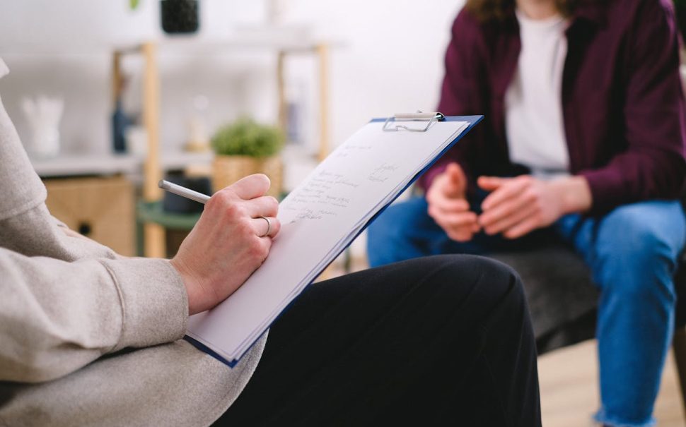 Writing notes on a clipboard while conversing with a patient.
