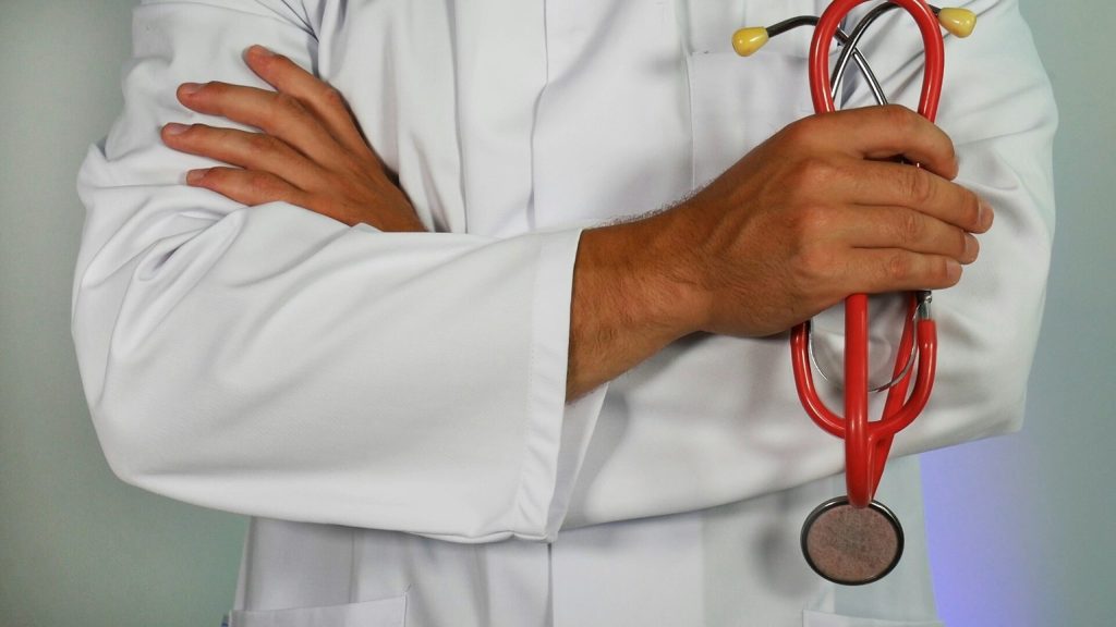 A doctor holding some equipment with crossed arms to with an article about NHS and immigration