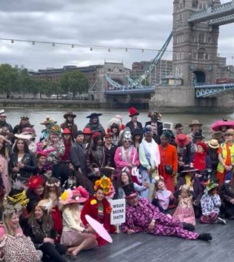 People wearing colourful hats and costumes gather by the Thames for a photo
