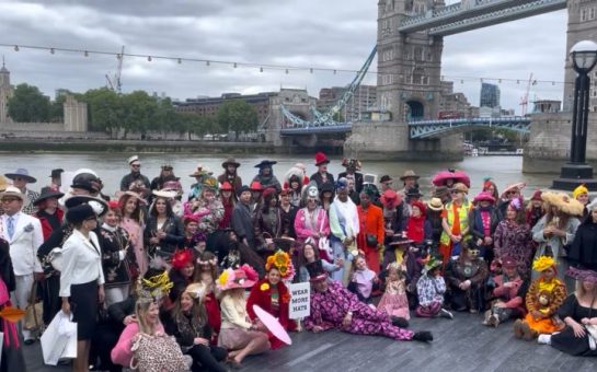 People wearing colourful hats and costumes gather by the Thames for a photo