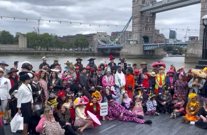 People wearing colourful hats and costumes gather by the Thames for a photo
