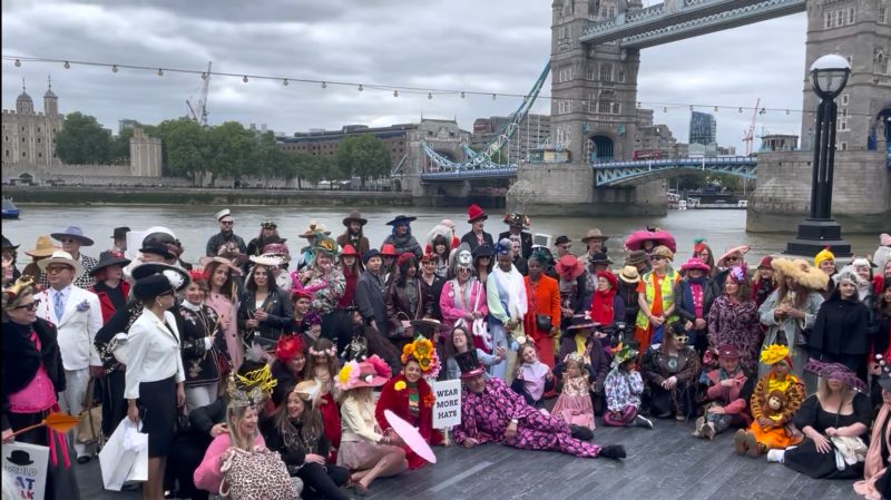 People wearing colourful hats and costumes gather by the Thames for a photo