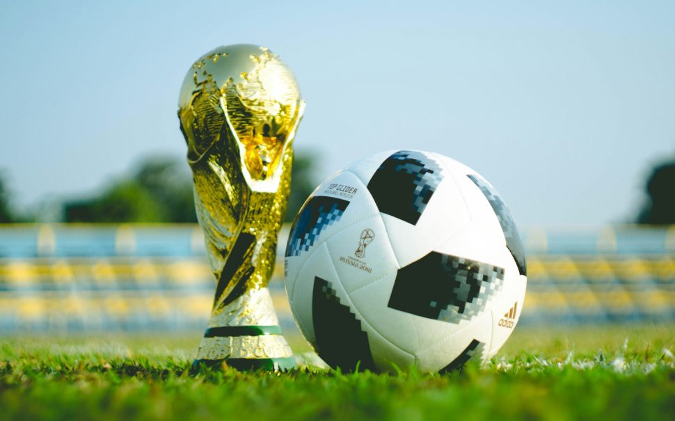 Football World cup trophy and ball on pitch.