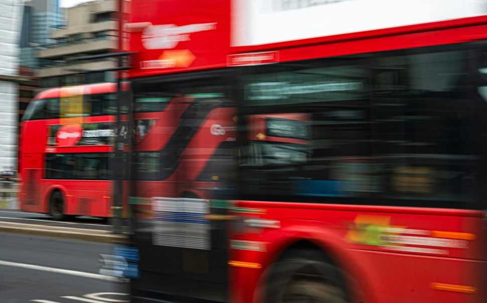 A blurry photo of red double decker buses driving down a road