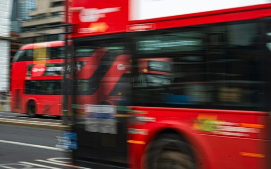 A blurry photo of red double decker buses driving down a road
