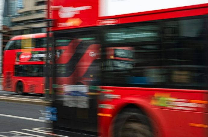 A blurry photo of red double decker buses driving down a road
