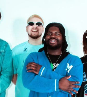 Four smiling boy band members dressed in blue.
