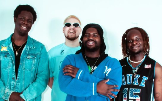 Four smiling boy band members dressed in blue.