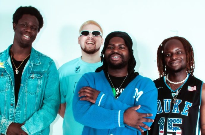 Four smiling boy band members dressed in blue.