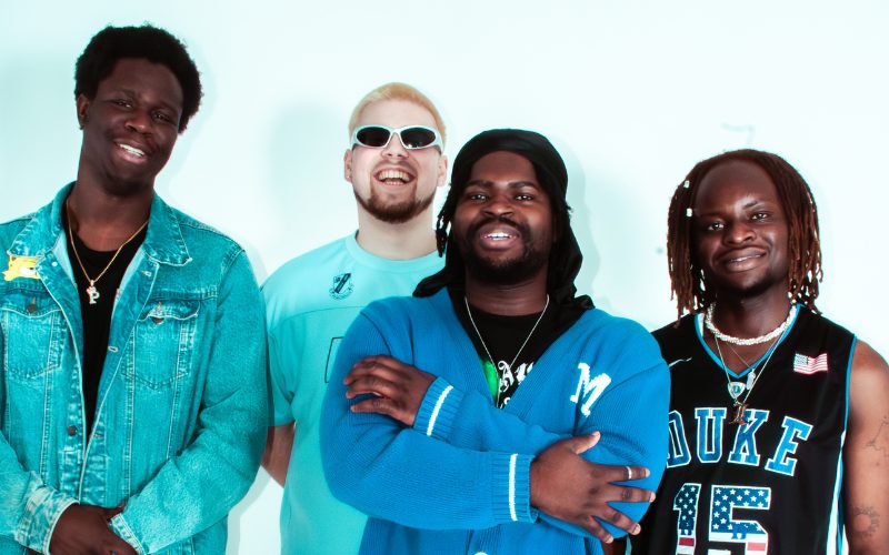 Four smiling boy band members dressed in blue.