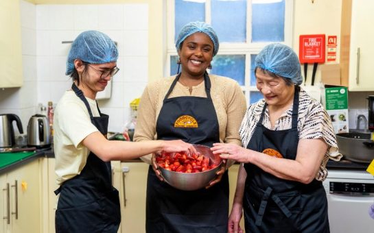 A photo of three volunteers in aprons that say 'FoodCycle' in the kitchen.