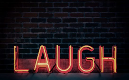 Red neon bar sign of the word LAUGH in capital letters for stand-up comedy story