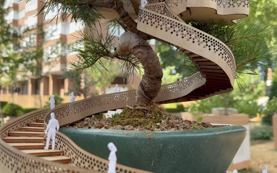 A bonsai tree with a wooden staircase wrapped around it with small plastic human figures on the steps