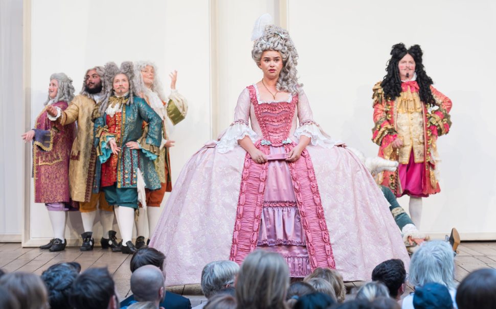 A leading actress stands at the front of the stage at Shakespeare's Globe in a regency era gown.