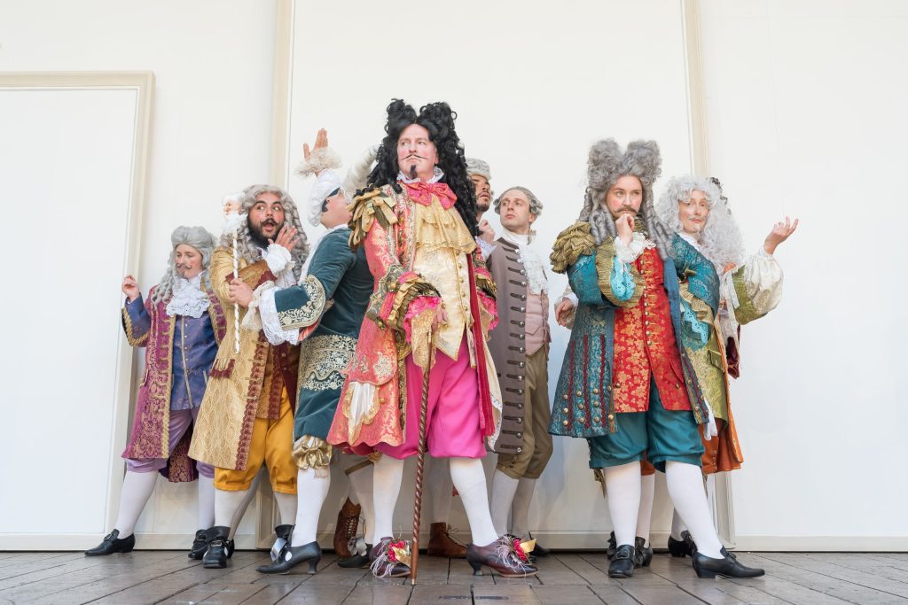 Members of the court stand in their finery on the stage of Shapeare's Globe theatre.