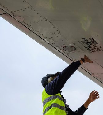 A man in a high vis jacket fixing the underside of a plane wing