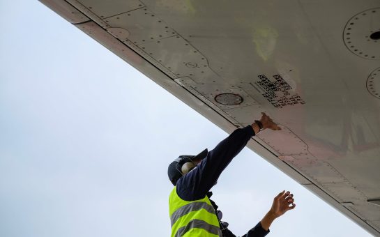 A man in a high vis jacket fixing the underside of a plane wing