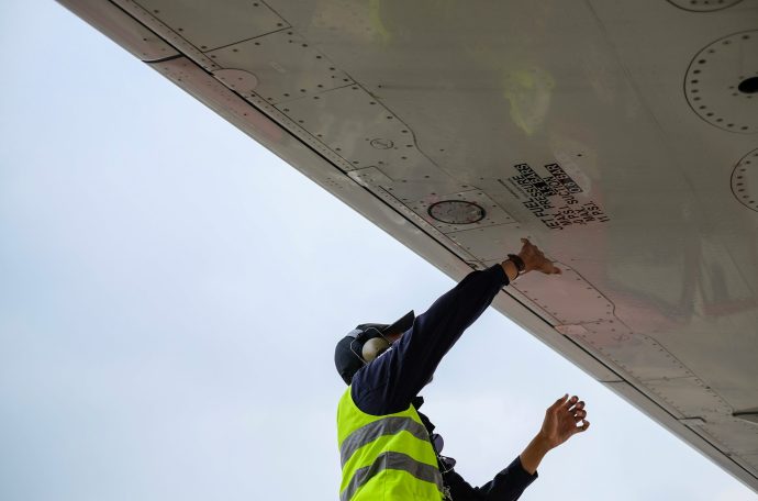 A man in a high vis jacket fixing the underside of a plane wing