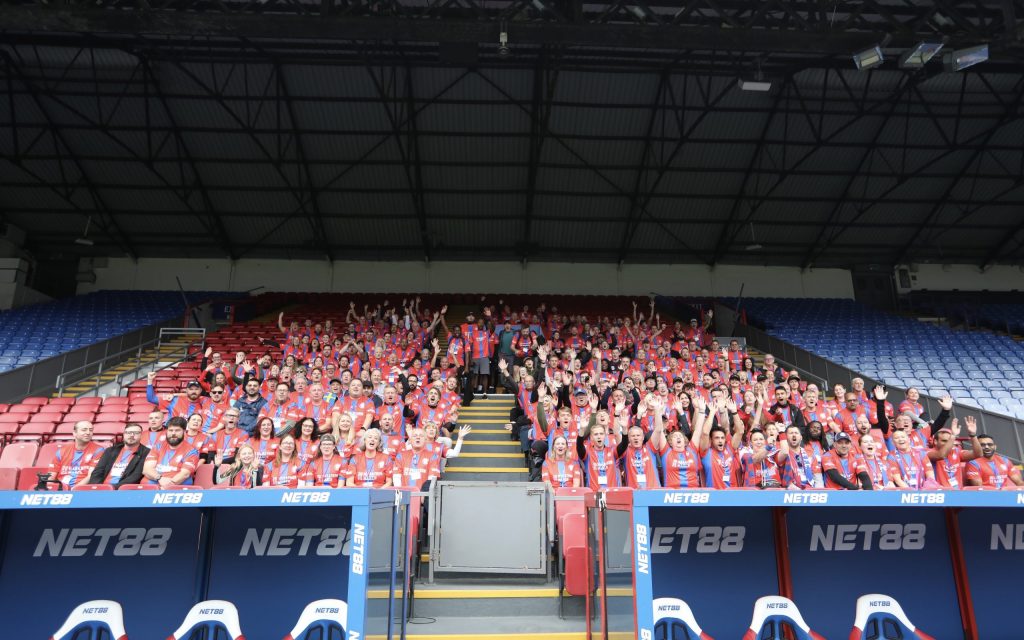 Marathon March walkers pose for photo in Selhurst Park stand with arms raised and smiles before March last year.