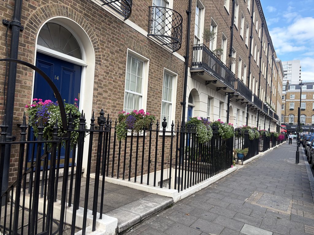 Rows of colourful flower planters attached to railings outside Marylebone townhouses.