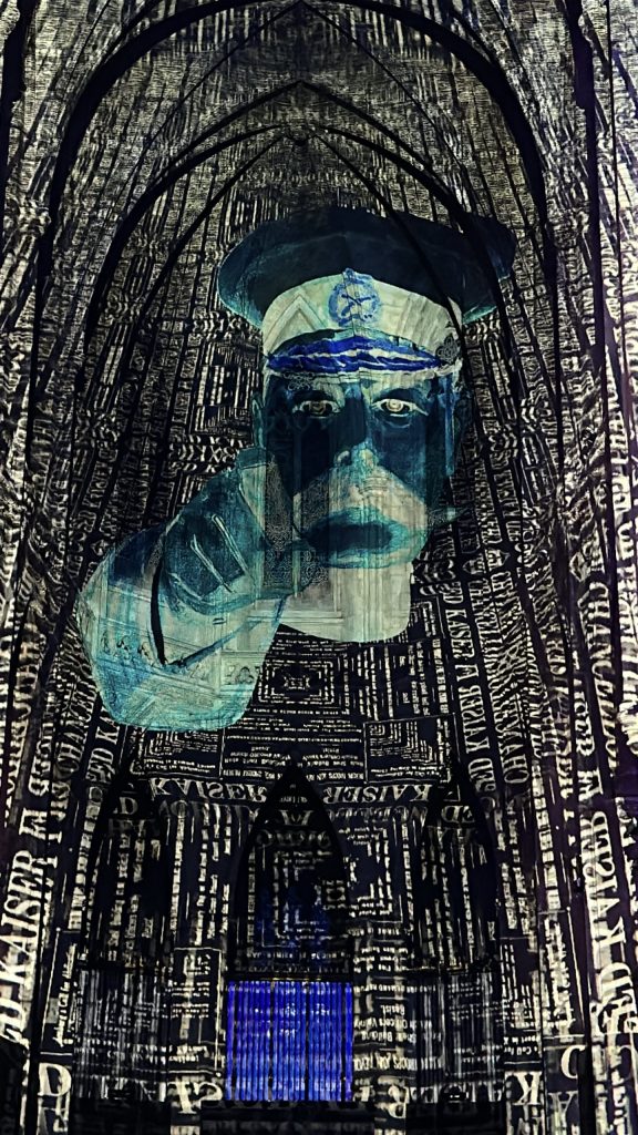 The walls of the building are dark but covered from floor to ceiling in white block text. In the centre, on top of the text, is a military personnel in inverted blue colours pointing towards the audience.
