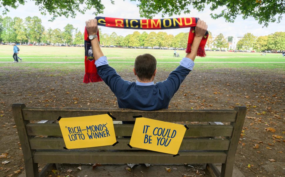 Man waves football scarf next to banners encouraging people to come forward as the mystery millionaire