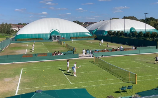 A high angle view overlooking the tennis courts at Raynes Park, with kids playing alongside coaches.