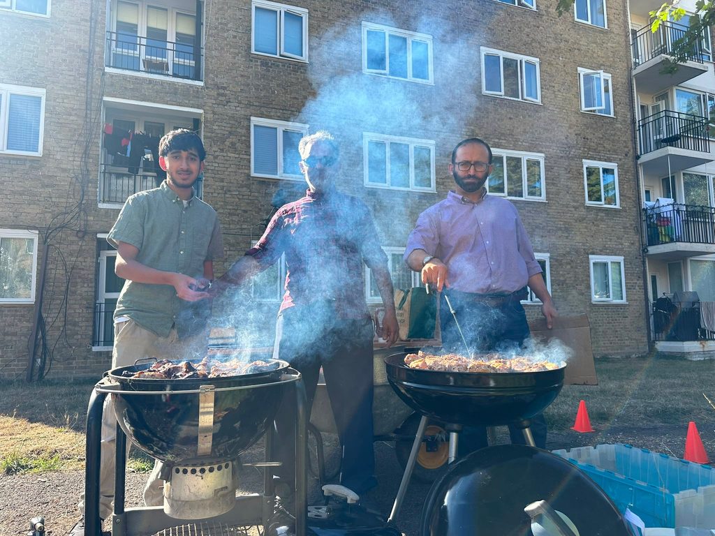 Three people, including father and son and the local councillor, preparing the barbecue for the party.