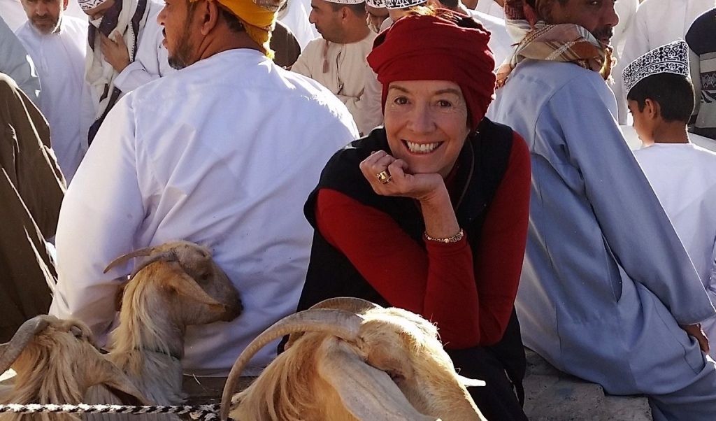 An image of Catherine DeVrye smiling among a group of male locals, posing for the camera near some goats.