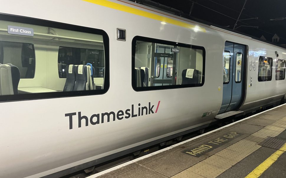 Photograph of a Thameslink Class 700 train, taken at night. The side of a white train carriage and blue sliding doors are visible.