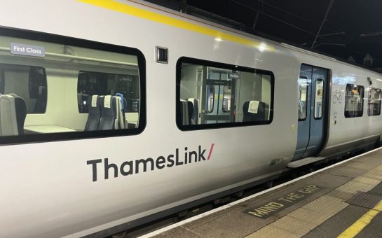 Photograph of a Thameslink Class 700 train, taken at night. The side of a white train carriage and blue sliding doors are visible.